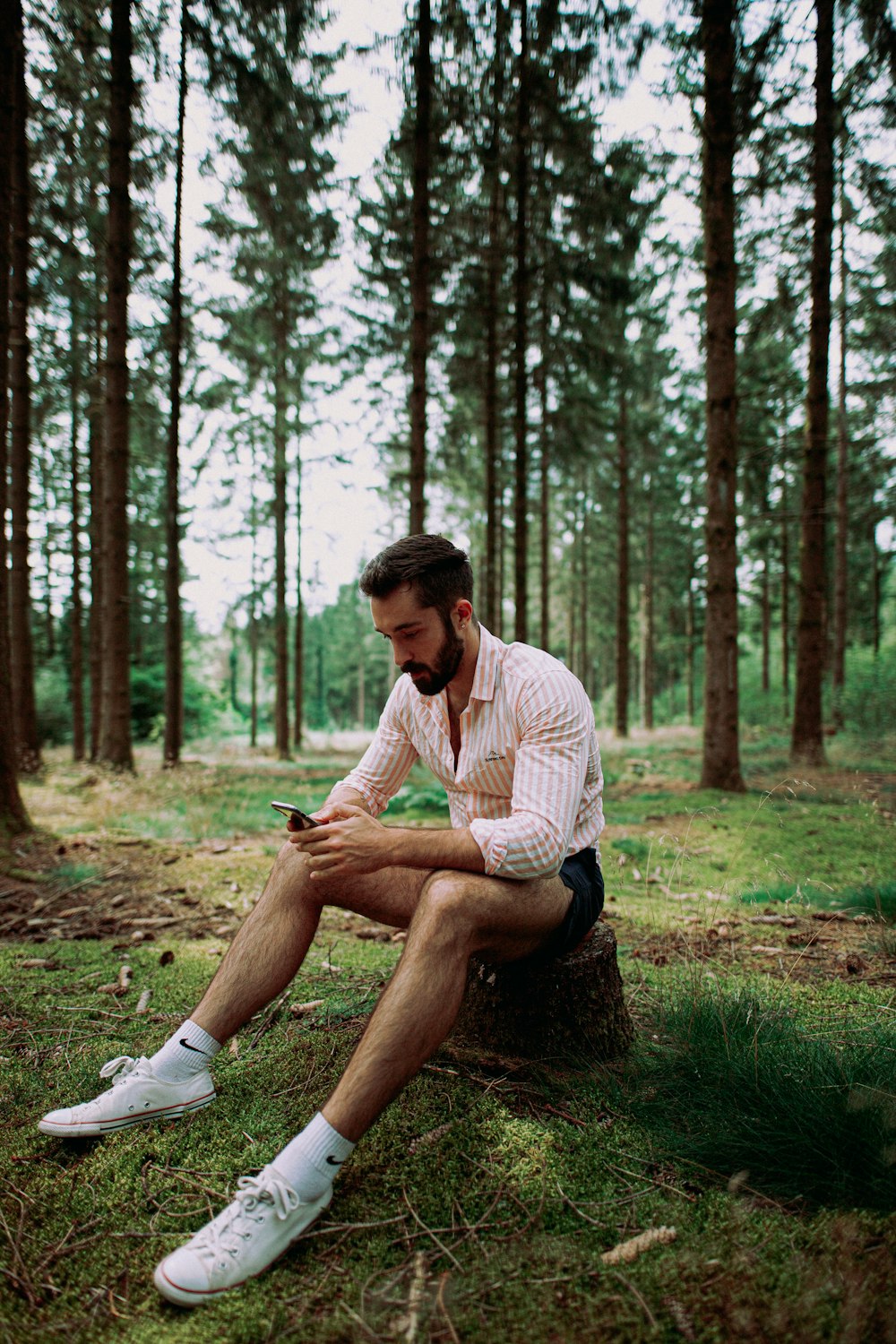 man in white and gray stripe dress shirt sitting on green grass field surrounded by trees