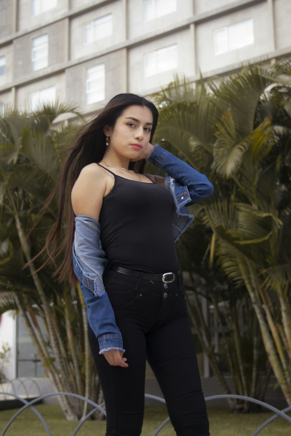 woman in black tank top and blue denim jeans standing near green palm tree during daytime