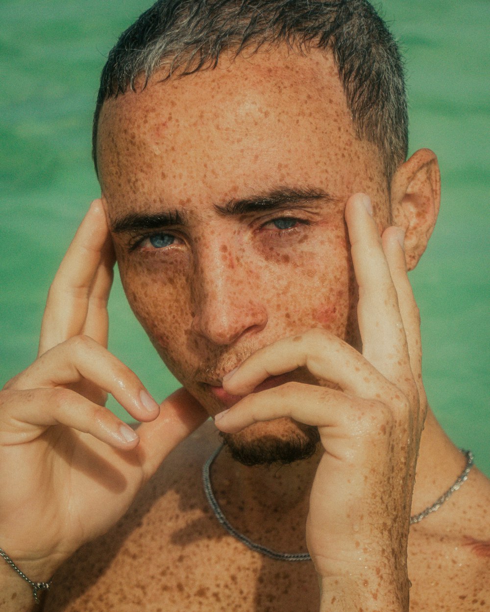 man in silver necklace covering his face with his hand