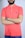 A person is standing with arms crossed wearing a coral polo shirt and a watch on their wrist. The logo on the shirt is blue and features a small bird.