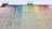 A large wall features flowing streaks of paint in rainbow colors, with each hue blending into the next. The paint appears to have dripped from the roof, creating an abstract, artistic pattern. The building structure includes two ladder-like elements at the top.