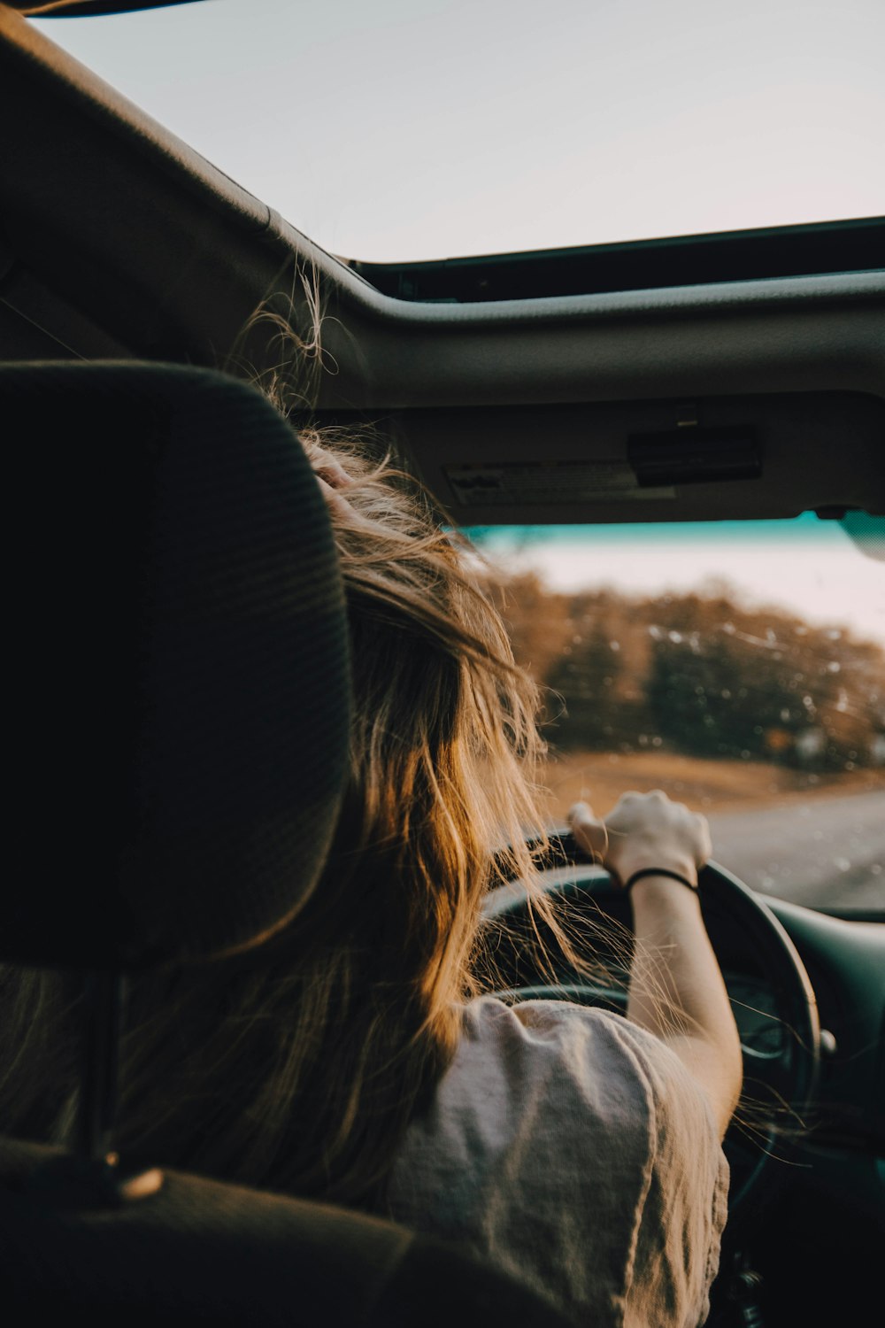 woman in gray jacket driving car during daytime