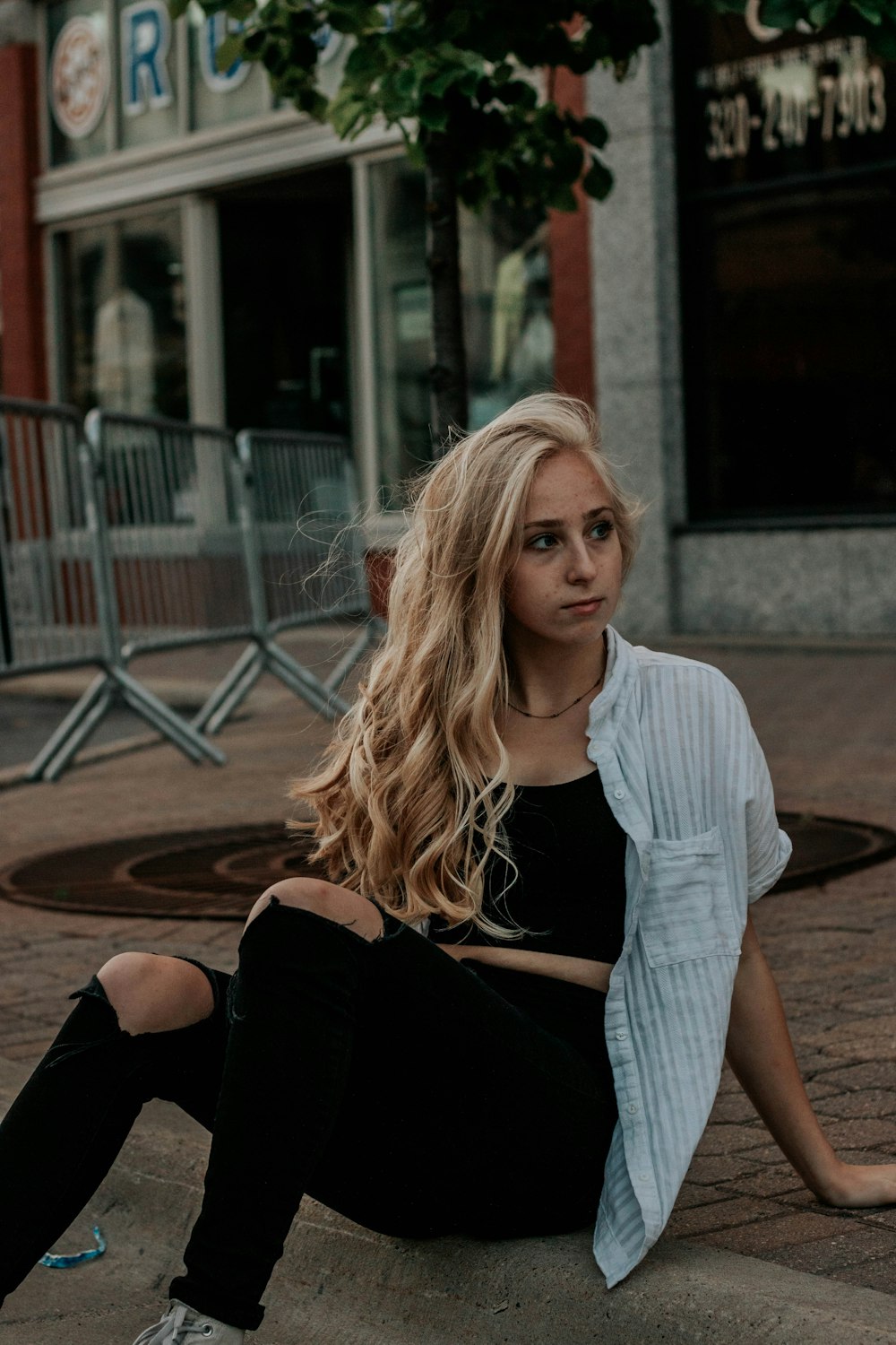 woman in white and black striped scoop neck shirt and black pants sitting on brown concrete