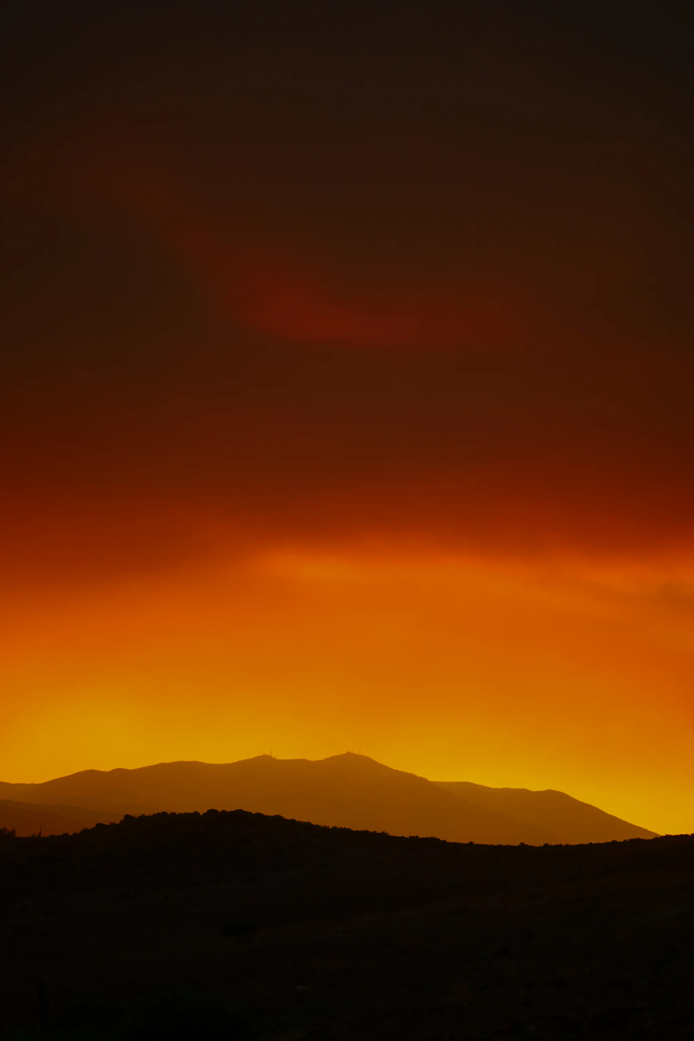 A dark mountain ridge silhouetted against an orange desert sunset