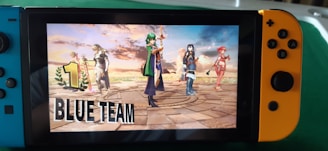 A Nintendo Switch console displays a victory screen from a video game, featuring animated characters standing triumphantly on a stone platform with a dramatic sky in the background. The words '1 Blue Team' are prominently displayed on the screen.