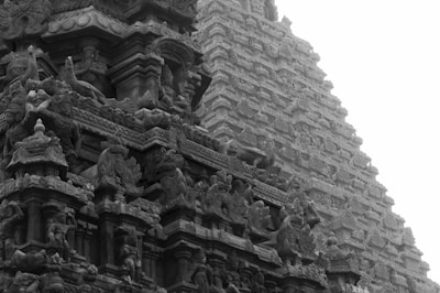 Elaborate stone carvings on an ancient temple facade, featuring intricate sculptures of deities and mythological figures. The architectural details display a high level of craftsmanship, with tiered structures and ornate patterns.