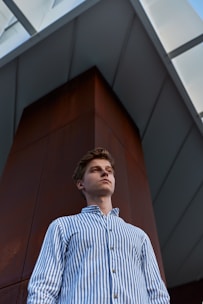 man in blue and white striped dress shirt standing near brown wall