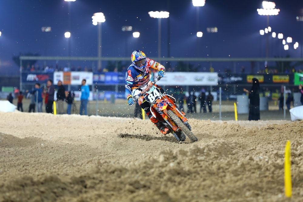 man in blue and white jacket riding orange motocross dirt bike during nighttime