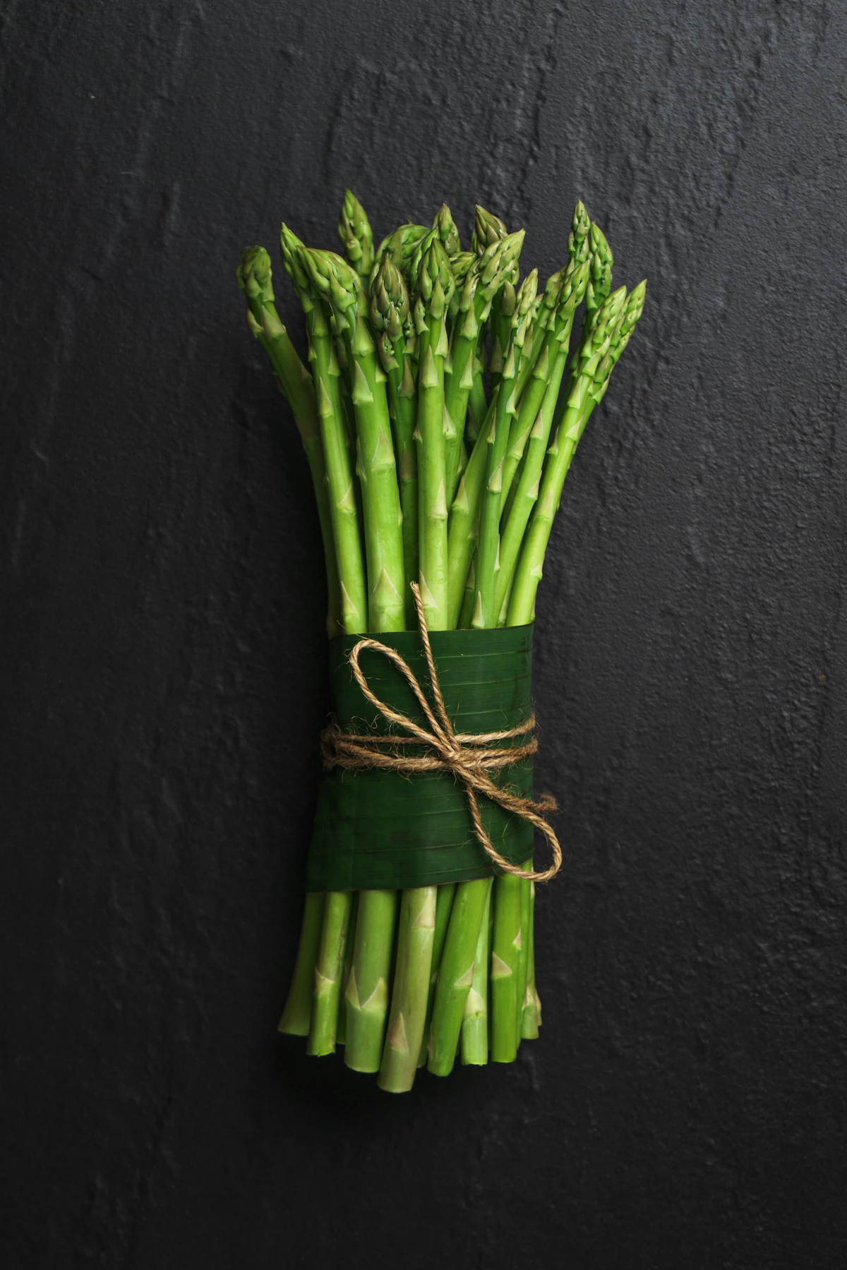 Bundle of fresh British asparagus spears tied with twine on dark slate - British asparagus recipes