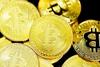 Several gold coins with the Bitcoin symbol prominently displayed across their surfaces. The coins are layered and overlapping, creating a rich and textured appearance.