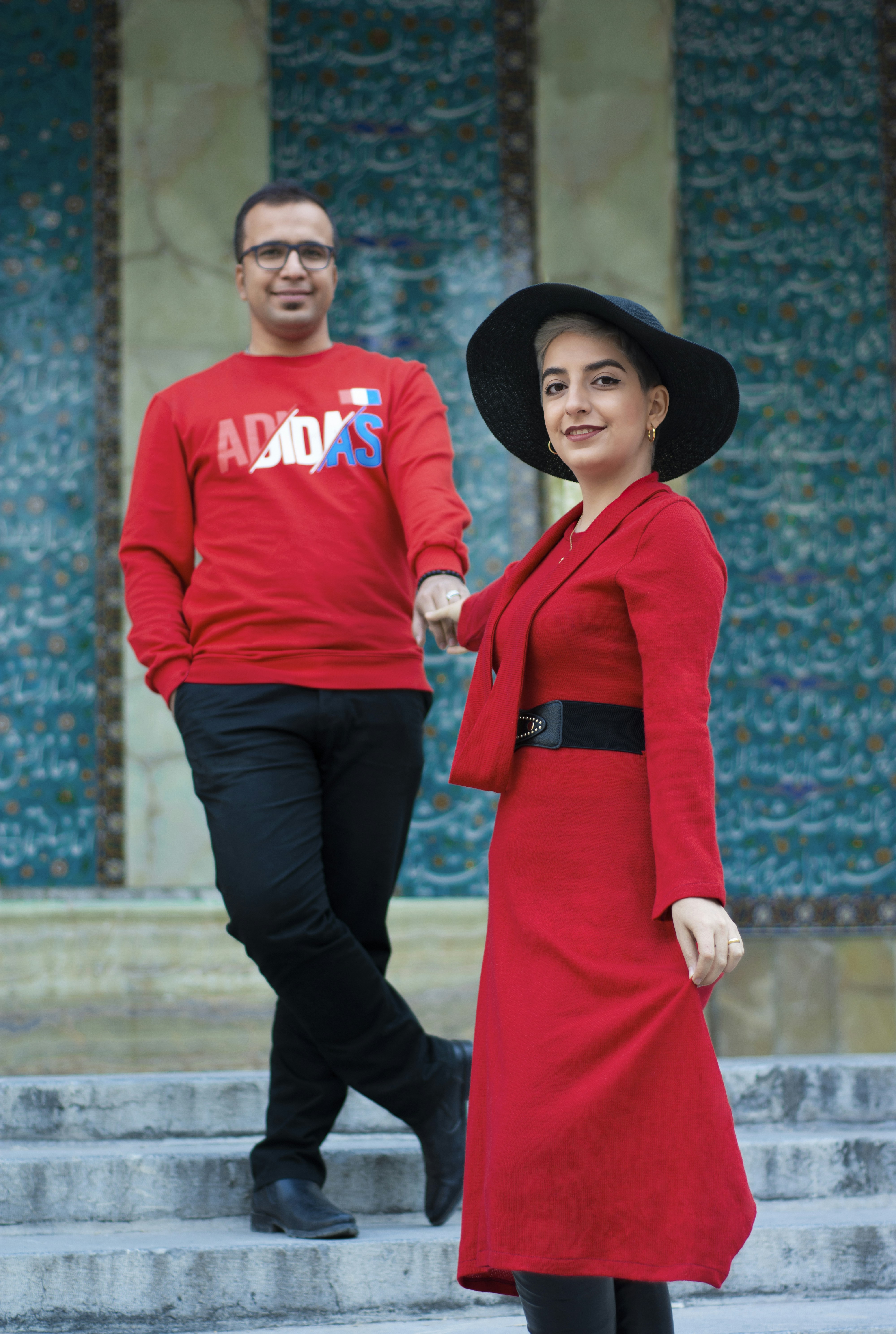 man in red long sleeve shirt and black pants standing beside woman in black hat