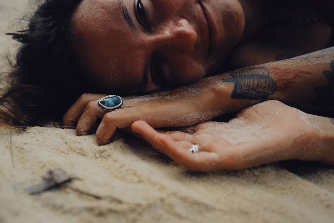 man lying on sand with silver ring