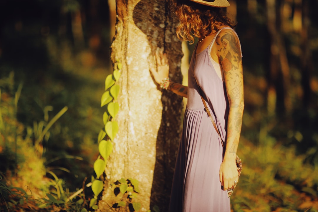 woman in white sleeveless dress wearing brown hat standing beside brown tree