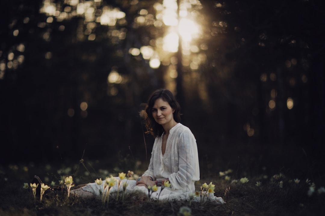 woman in white long sleeve shirt sitting on green grass during daytime