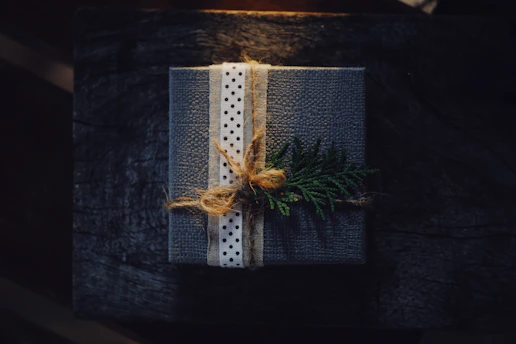 A cozy gift-wrapped box with a soft ribbon, resting on a wooden table surrounded by delicate flowers.