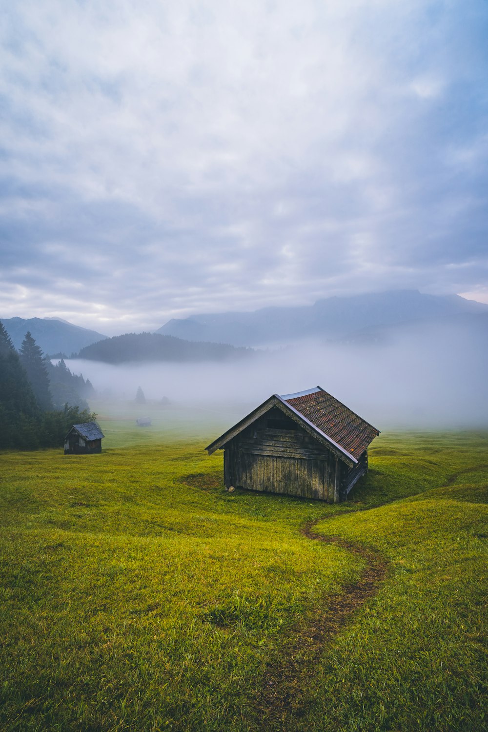 brown wooden house on green grass field near mountains under white clouds during daytime