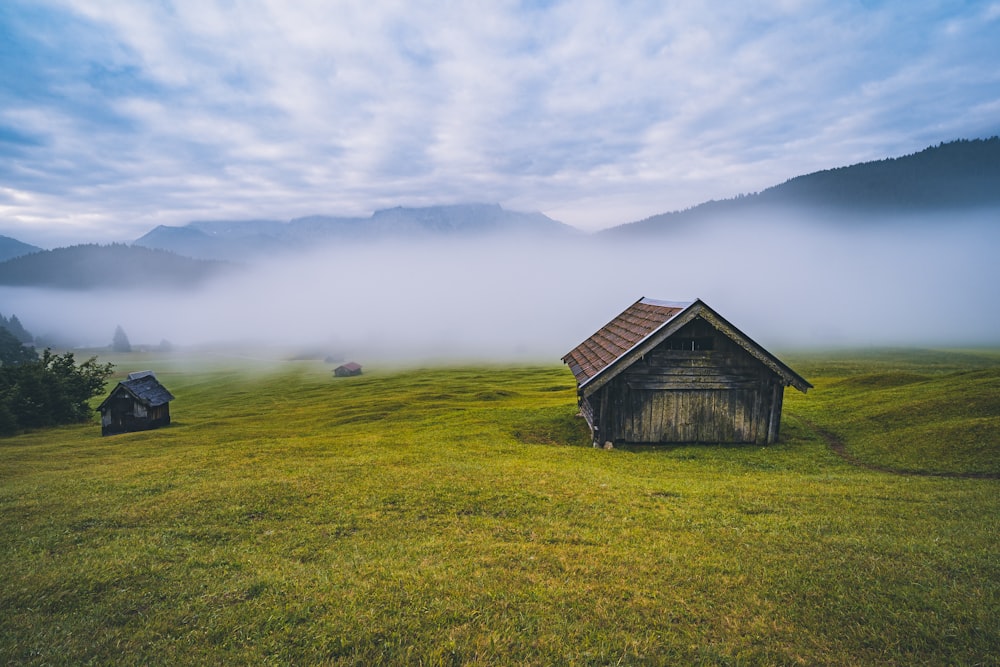 maison en bois marron sur un champ d’herbe verte sous des nuages blancs pendant la journée