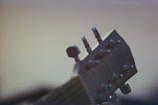 A close-up of the tuning pegs on the headstock of a guitar, with a soft focus on the wooden material and metallic tuners. The background is blurred, emphasizing the details of the guitar's head.