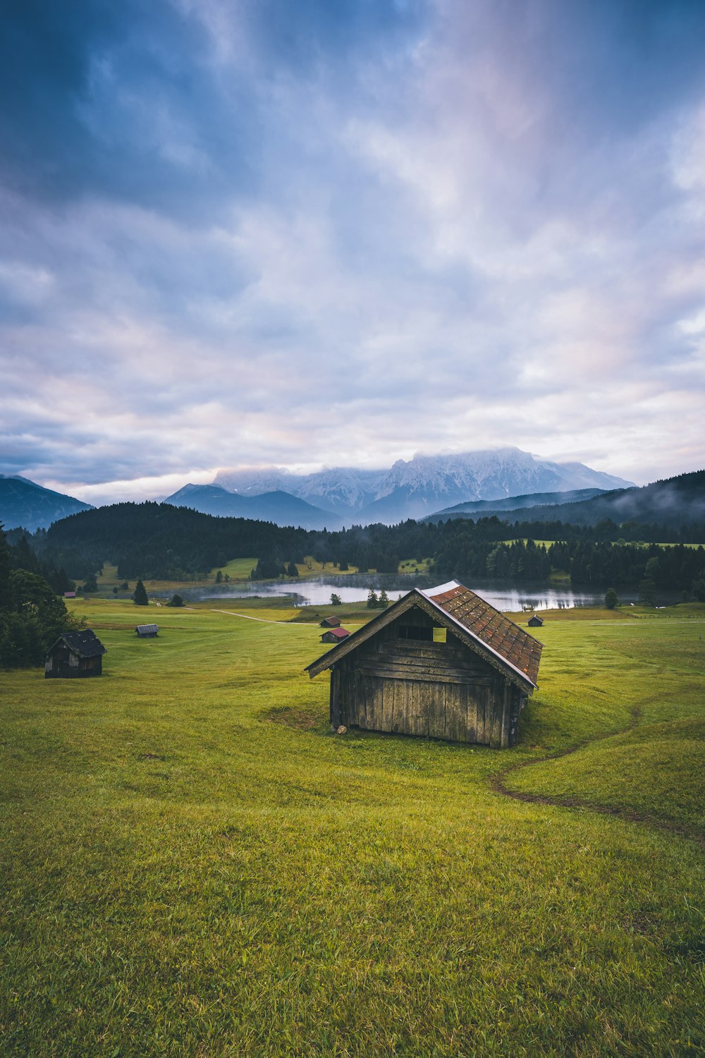 Braunes Holzhaus auf grünem Grasfeld in der Nähe von Green Mountains unter weißen Wolken und blauem Himmel