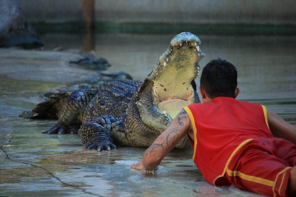 boy in orange t-shirt and brown pants sitting on brown crocodile on water during daytime