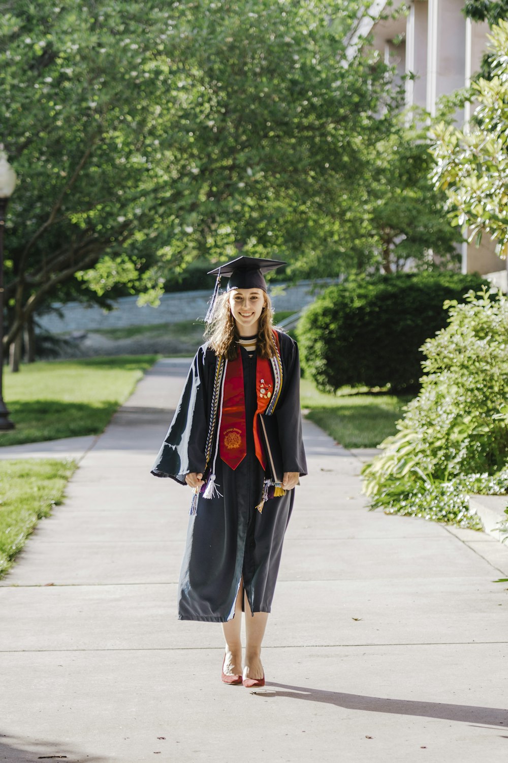 woman in black academic dress and black academic dress standing on gray concrete pathway during daytime