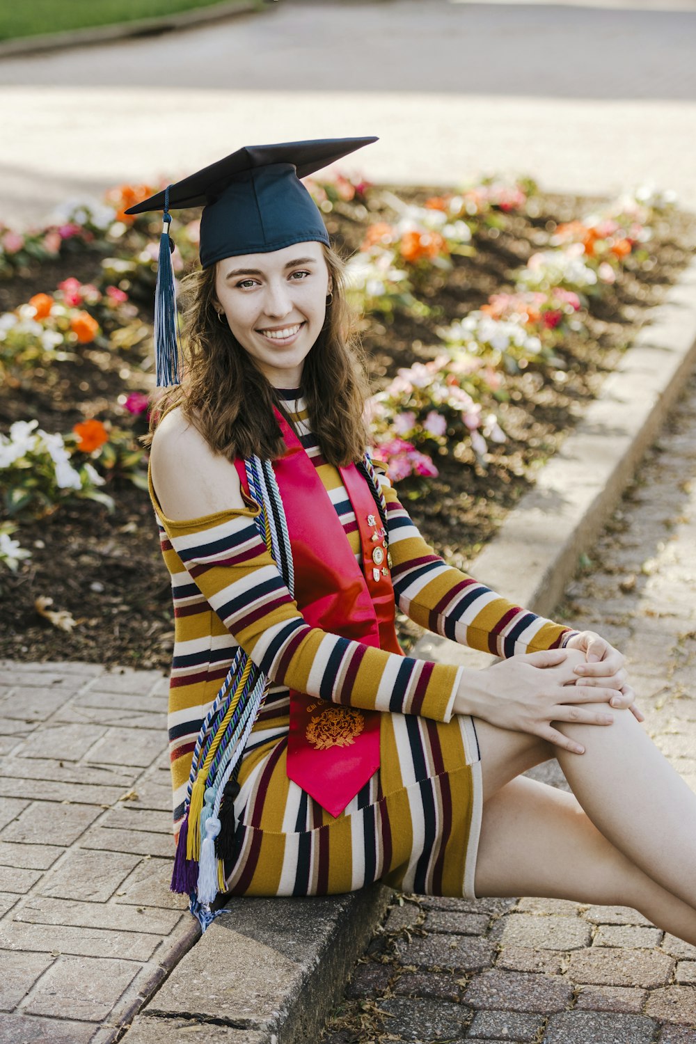 woman in red yellow and black stripe sleeveless dress sitting on concrete pavement