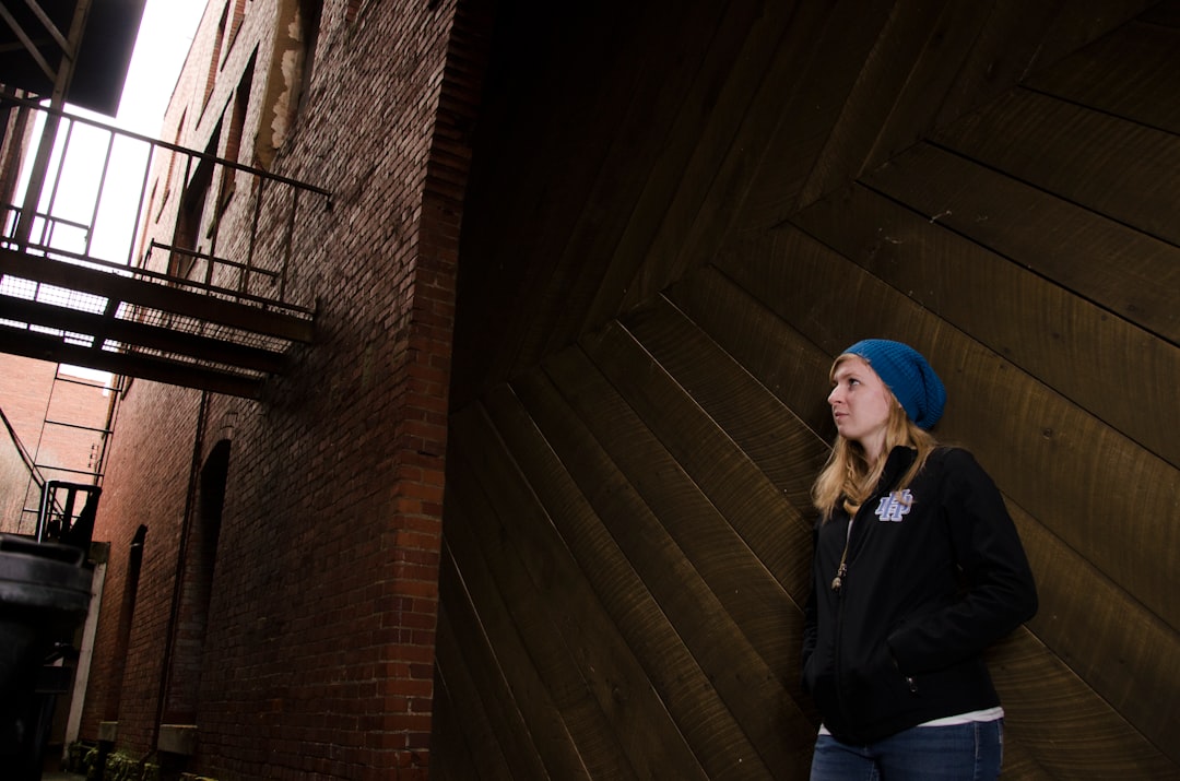 woman in black jacket and blue knit cap standing on brown wooden stairs