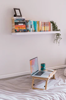 A calm, neutral-toned room featuring a tidy bookshelf and a laptop ready for online learning.