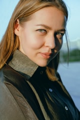 A close-up portrait of a woman with natural light highlighting her features in a charcoal grey background