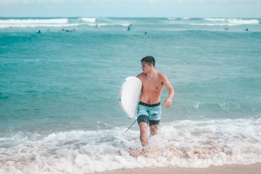 man in blue denim shorts holding white surfboard on beach during daytime