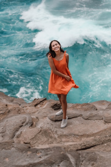 A joyful woman standing on a sunlit cliff overlooking the ocean, her backpack ready for the next adventure.