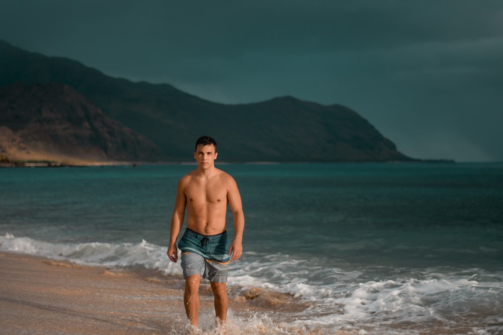 topless man in blue denim shorts standing on seashore during daytime