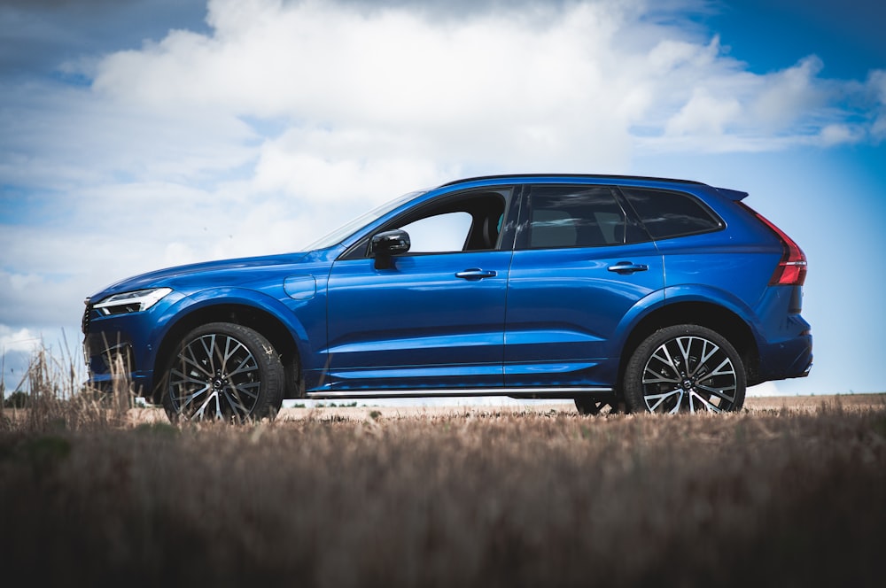 blue car on brown grass field under white clouds and blue sky during daytime