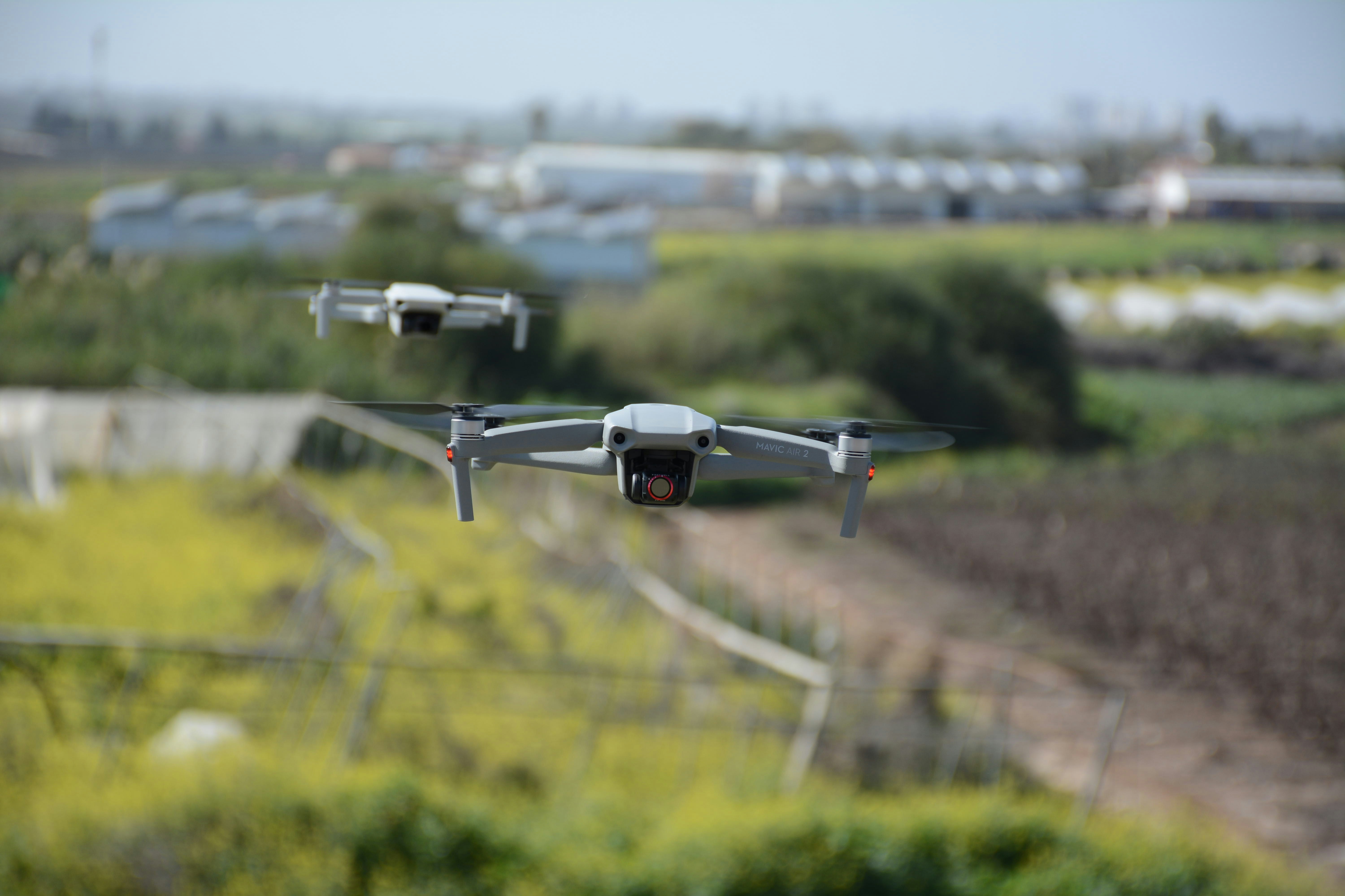 Drone bianco e nero che vola sopra il campo di erba verde durante il giorno