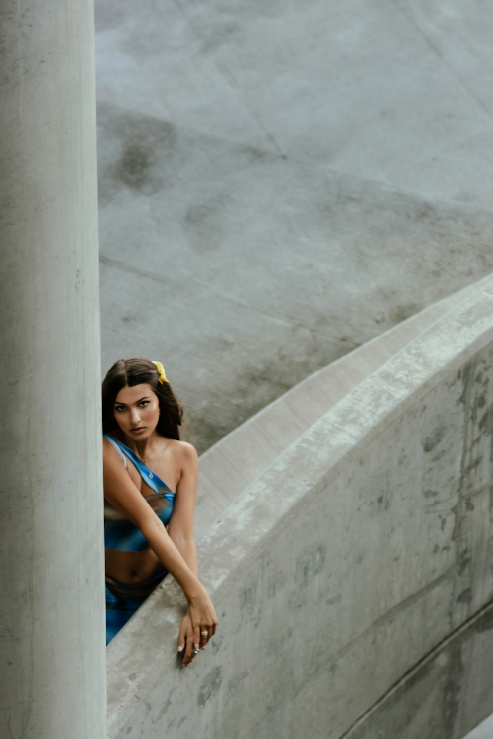 woman in blue tank top leaning on gray concrete wall