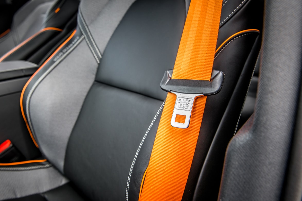 An orange seat belt against the leather interior of a car.