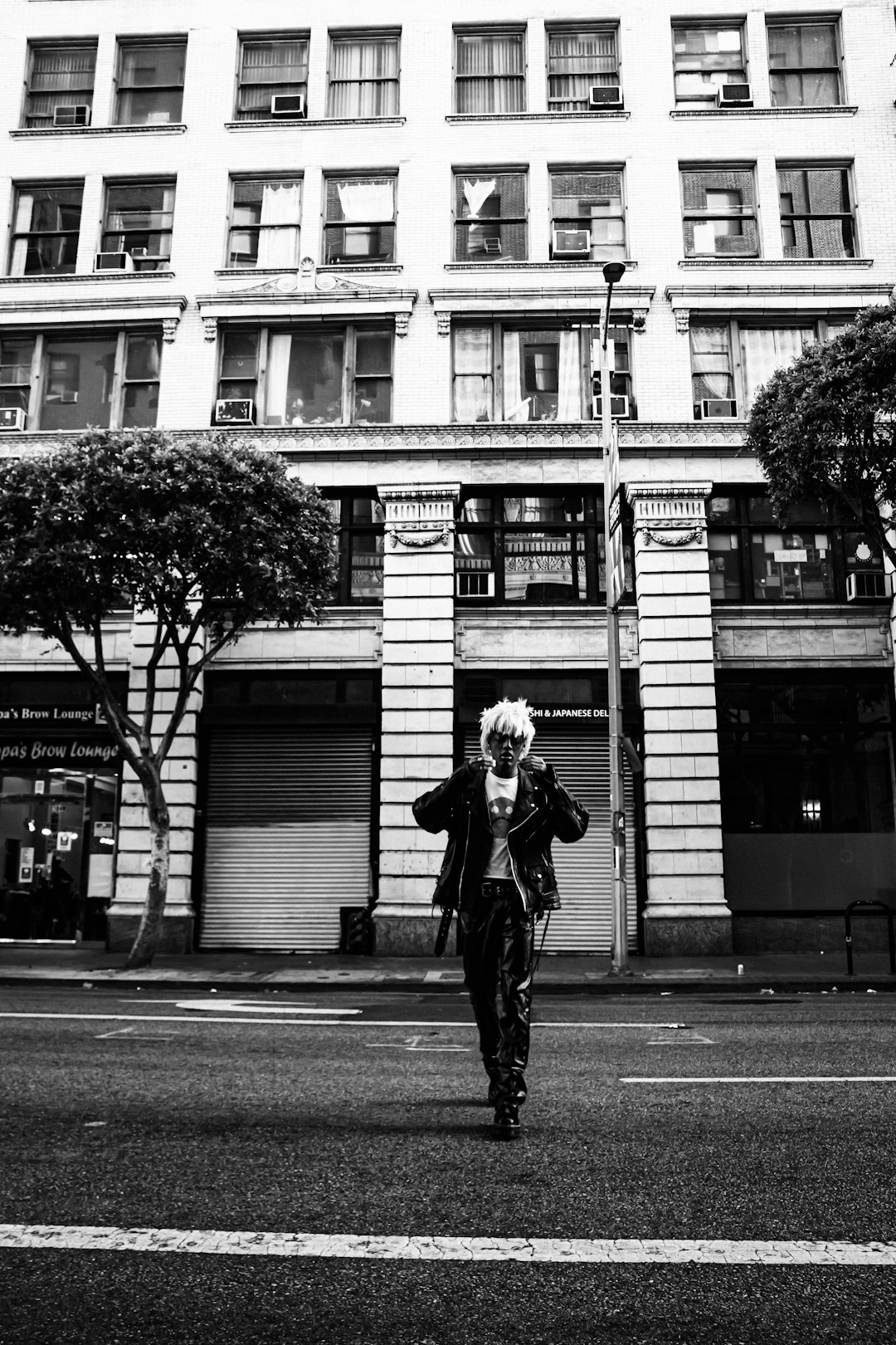 grayscale photo of woman in black jacket and pants standing on sidewalk