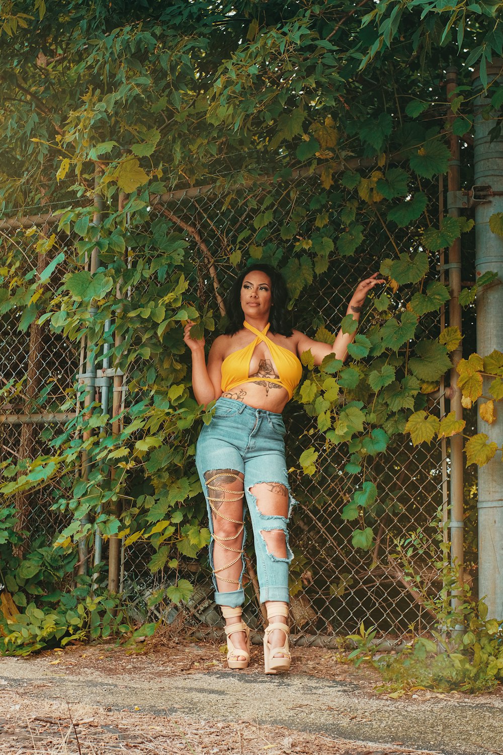 woman in yellow tank top and blue denim jeans leaning on gray metal fence