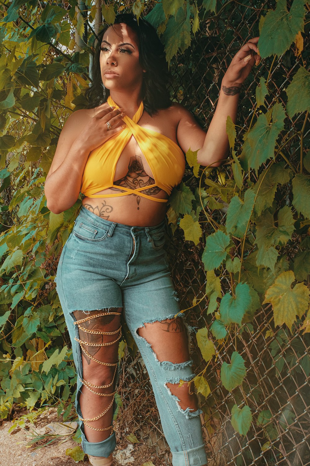 woman in yellow crop top and blue denim shorts standing beside green plants