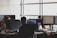 Several people working at desks with computer monitors, focusing on programming and other tasks. The office space is bright with natural light from large windows.