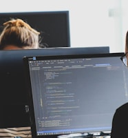 woman in black shirt sitting beside black flat screen computer monitor