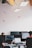 An office environment with multiple people working at desks equipped with computers. Hanging from the ceiling are small, model airplanes creating a whimsical touch. The lighting is provided by rectangular ceiling lights, and there are several computer monitors visible.