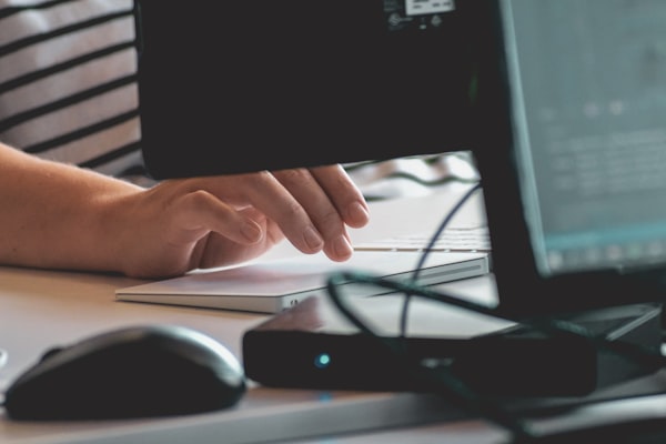 a person clicking a trackpad in front of a computer monitor