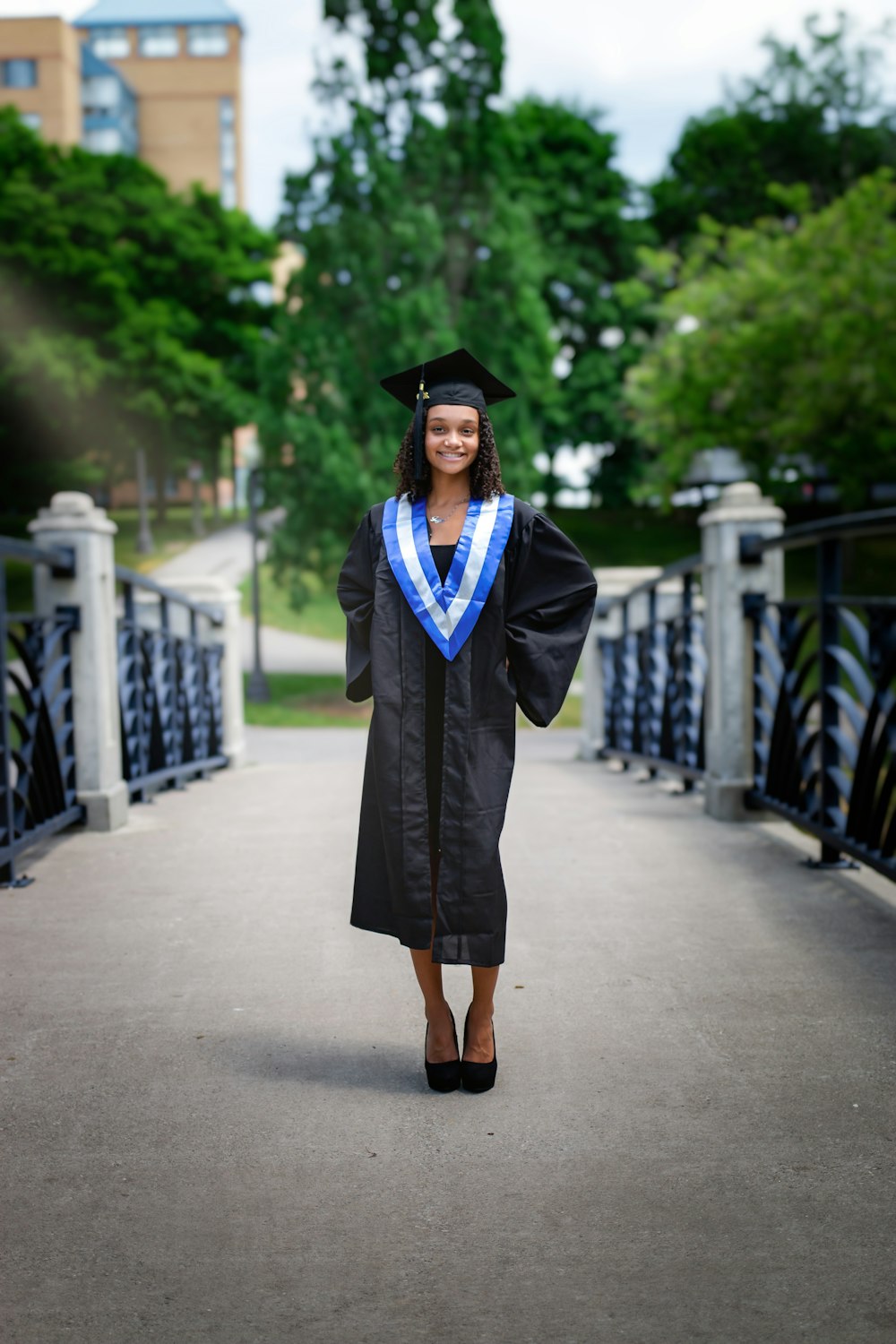 woman in black academic dress standing on gray concrete pathway during daytime