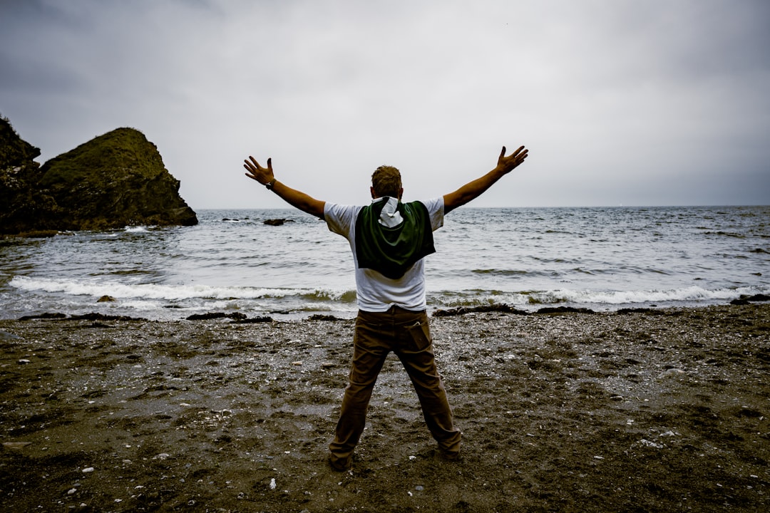 man in white and black hoodie standing on seashore during daytime