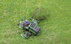 A friendly lawn care professional holding a mower, smiling in a freshly cut green yard.