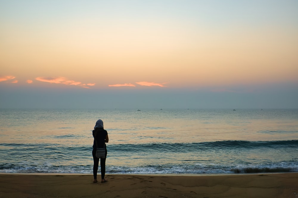 man in black jacket standing on beach during sunset