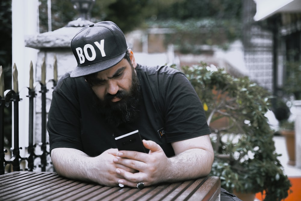 man in black shirt and black cap holding smartphone