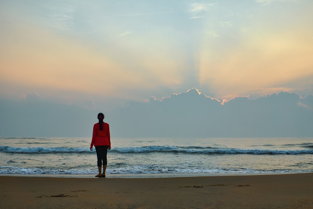 mulher na camisa vermelha da manga comprida em pé na praia durante o dia