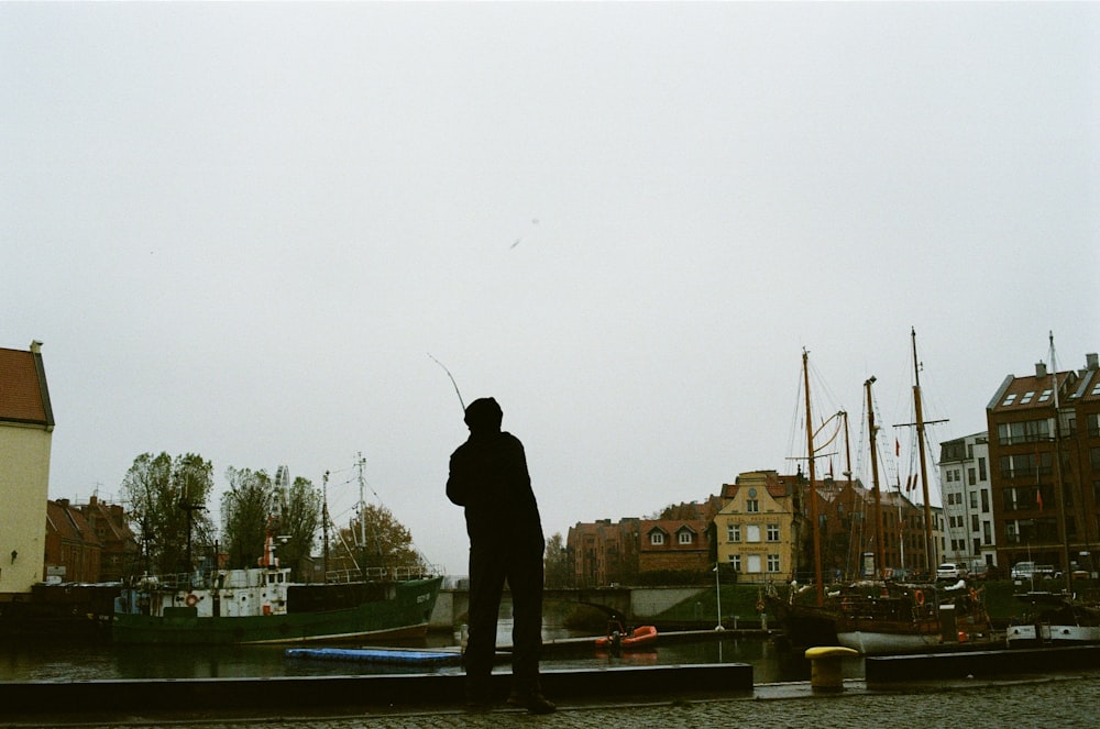 Hombre en chaqueta negra y pantalones de pie en el puente durante el día
